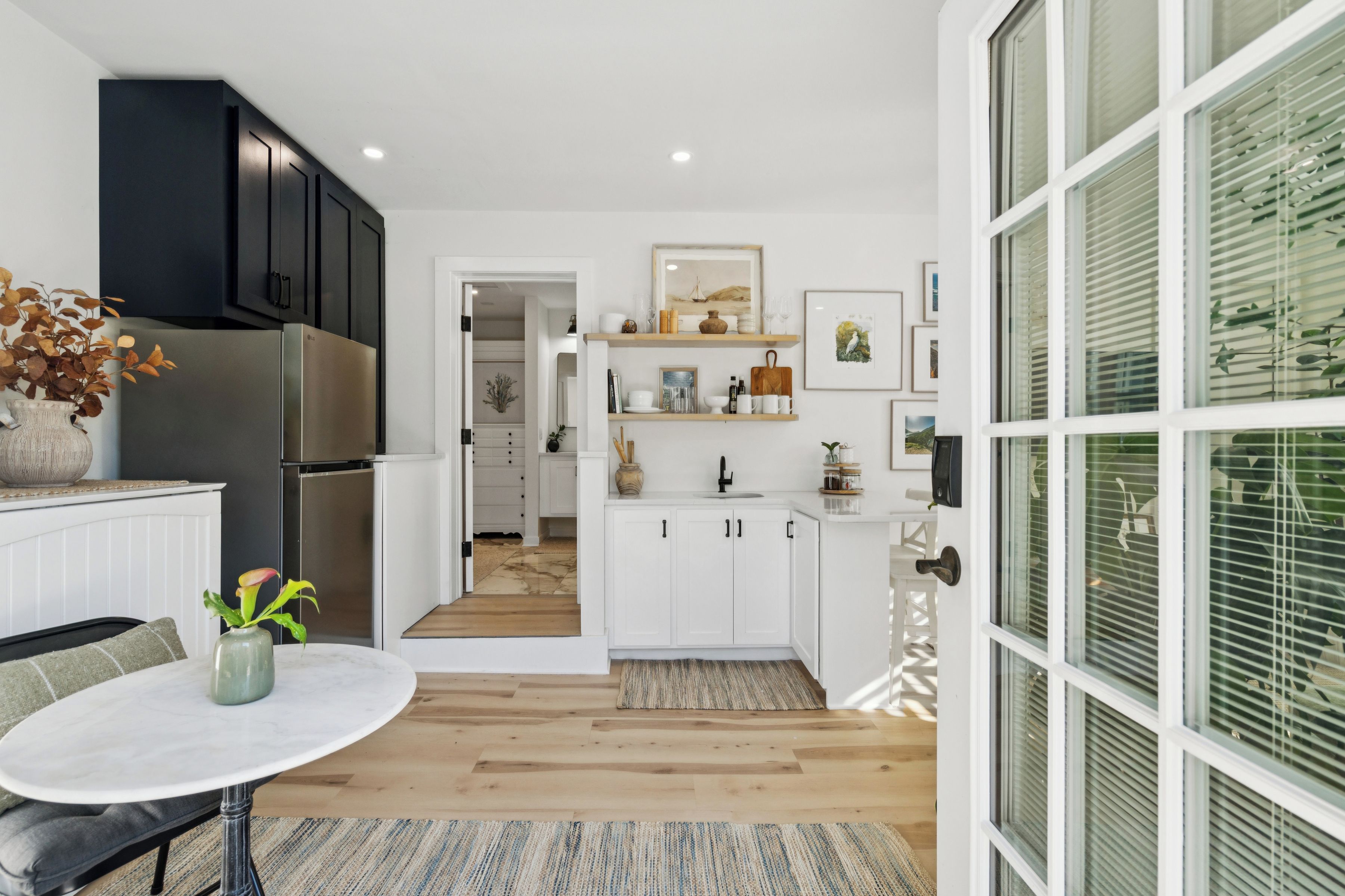 A modern kitchen with white cabinets, a stainless steel refrigerator, and a dining area with a round table.