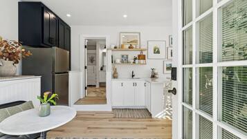 A modern kitchen with white cabinets, a stainless steel refrigerator, and a dining area with a round table.