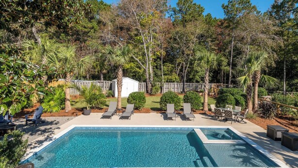 A rectangular swimming pool with a clear blue water surface, surrounded by a concrete deck. There are lounge chairs aligned along the pool's edge, and a small white shed is visible in the background. - Charming Upscale Beach House Suite - Cozy Coop (Mount Pleasant)