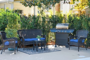 An outdoor patio with wicker furniture, a grill, and a blue rug.