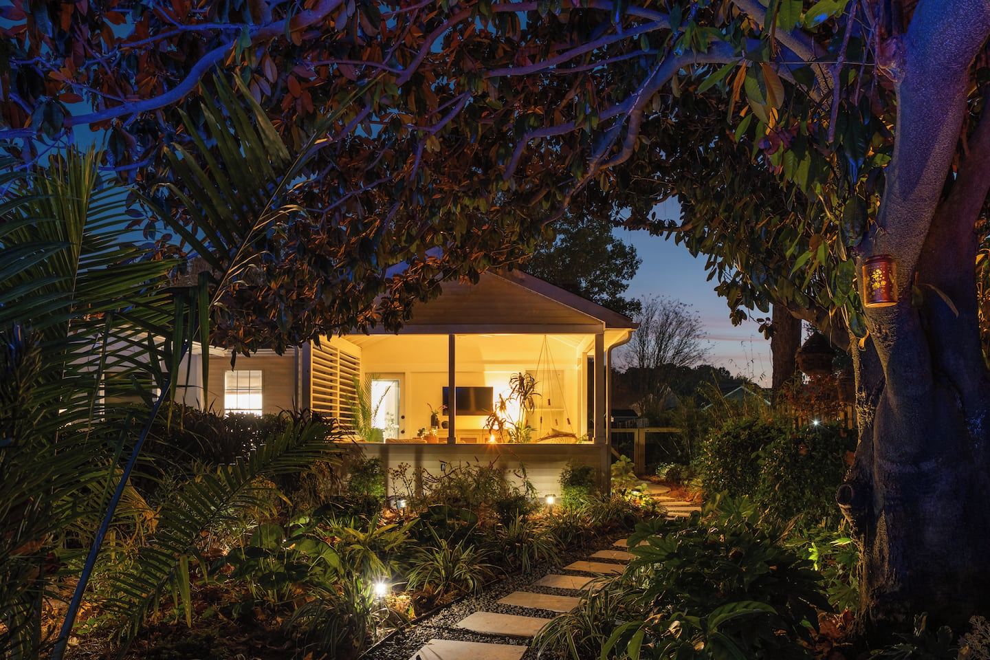 Une maison dotée d’un espace cuisine extérieure bien visible, entourée d’une végétation luxuriante et accessible par un chemin de pierre menant à l’entrée.