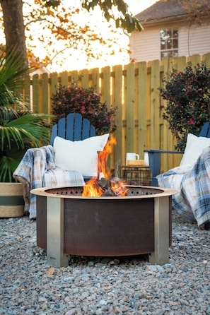 A fire pit with a metal frame and a flat top, surrounded by gravel.