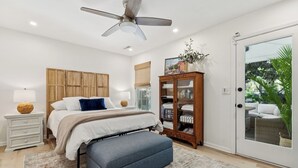 A bedroom with a bed, bedside tables, a wardrobe, a cabinet, a ceiling fan, and a view of the outdoors. - Charming Upscale Beach House Suite - Cozy Coop (Mount Pleasant)