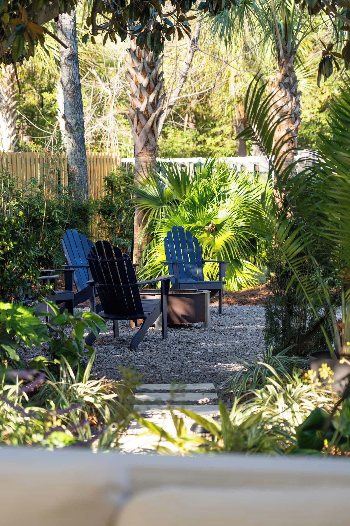 Ein Garten mit zwei Adirondack-Stühlen, einer Palme und einem Holzzaun.