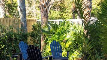 Ein Garten mit zwei Adirondack-Stühlen, einer Palme und einem Holzzaun.