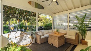 A sunroom with a ceiling fan, wicker furniture, and large windows. - Charming Upscale Beach House Suite - Cozy Coop (Mount Pleasant)