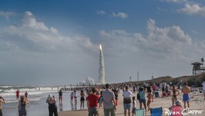 Ein Strand voller Menschen, ein Rettungsturm und ein Raketenstart.