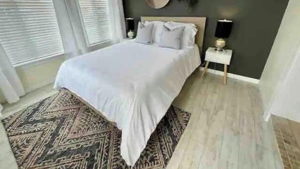 Ein Schlafzimmer mit einem Bett, einem Nachttisch, einer Wanduhr und einem Fenster mit Jalousien.