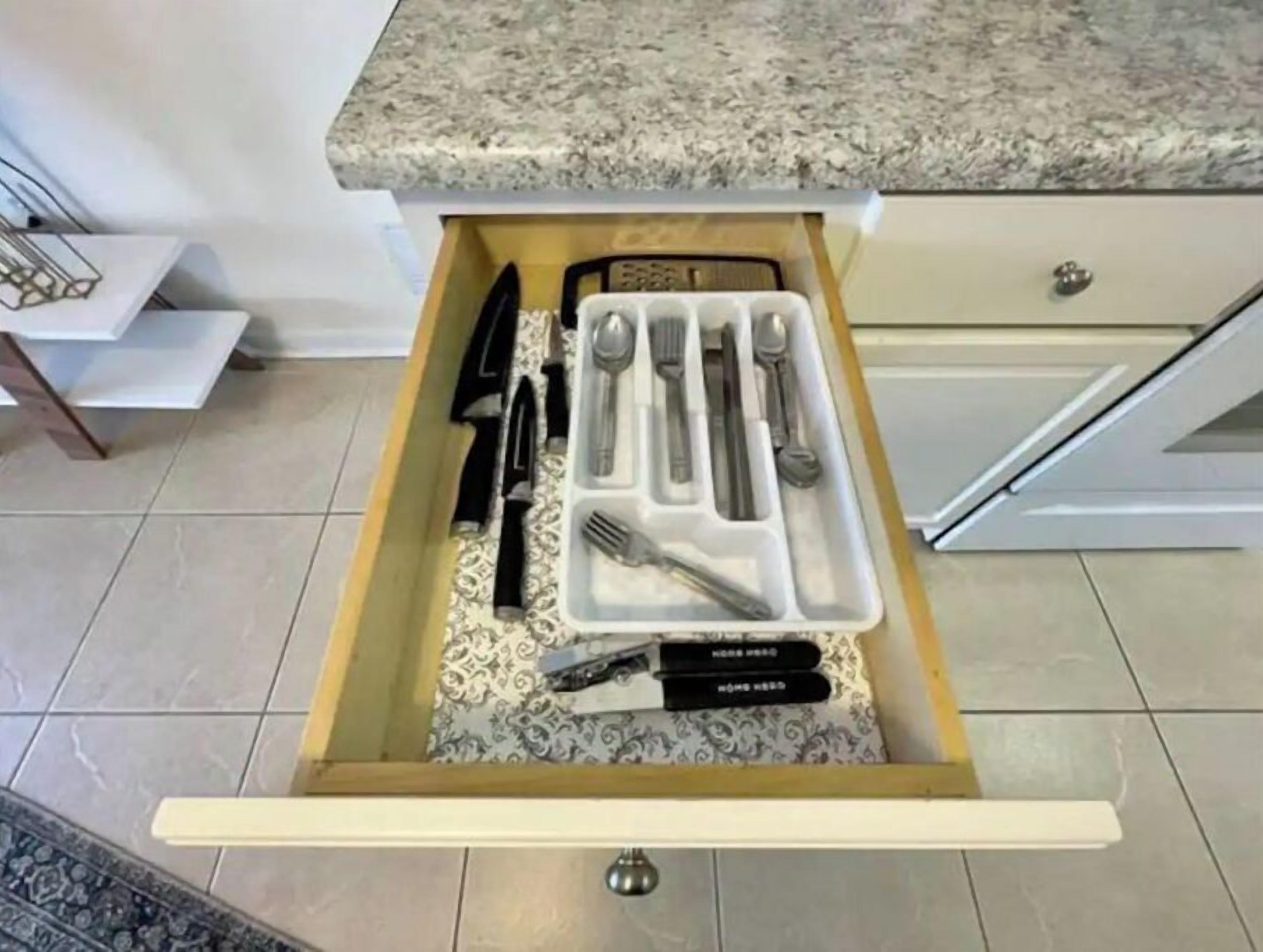 A kitchen drawer with utensils and a cookbook.