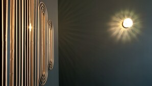 Una pared con varios apliques verticales metálicos, de forma ovalada, y una fuente de luz redonda e iluminada a la derecha.