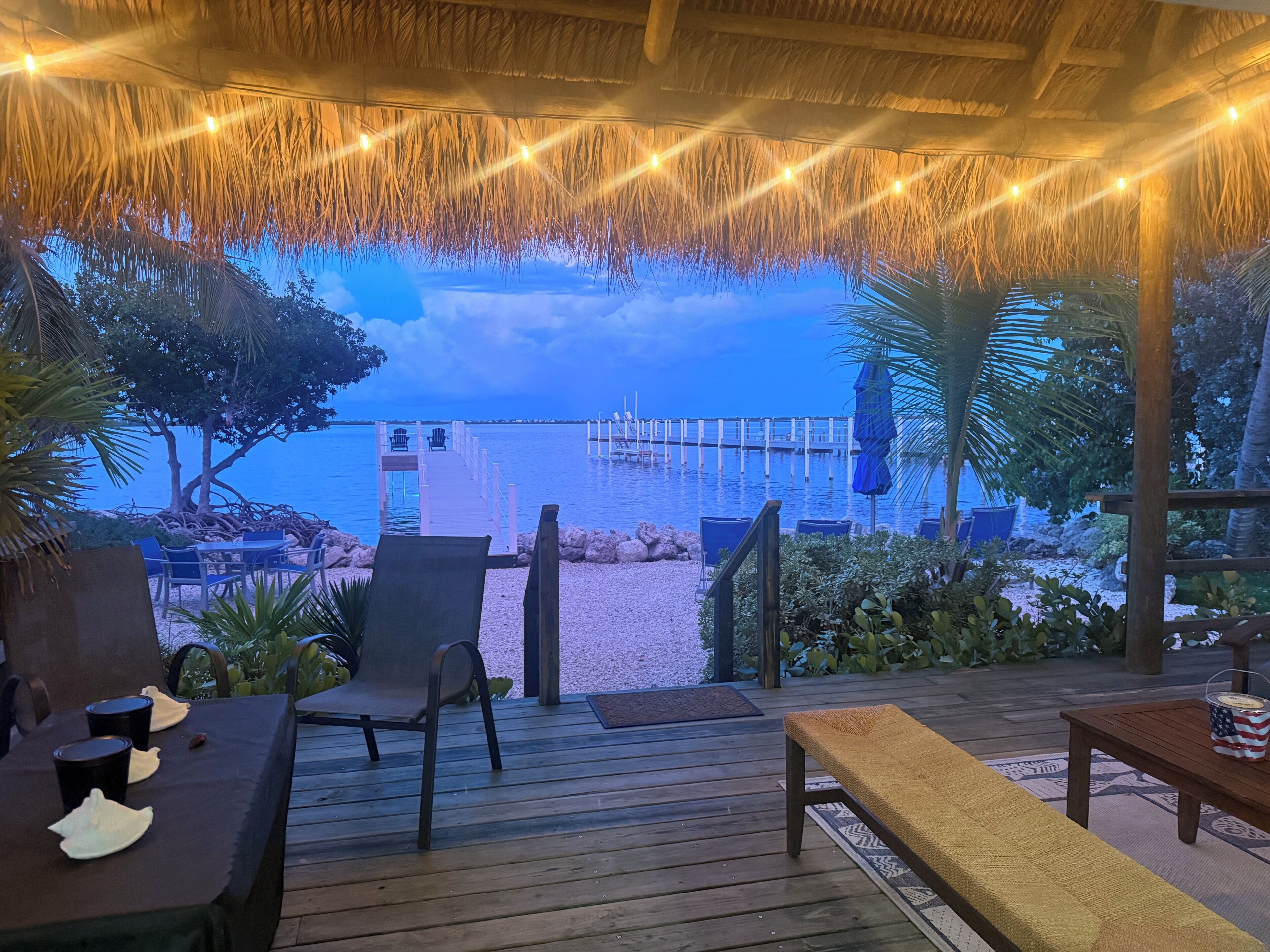 A wooden deck with outdoor seating, a thatched roof, and a view of the beach and pier.