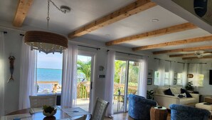 A spacious living room with a wooden ceiling, a dining area with a table and chairs, and a view of the sea through large windows. - Peaceful ocean front cottage. (Summerland Key)