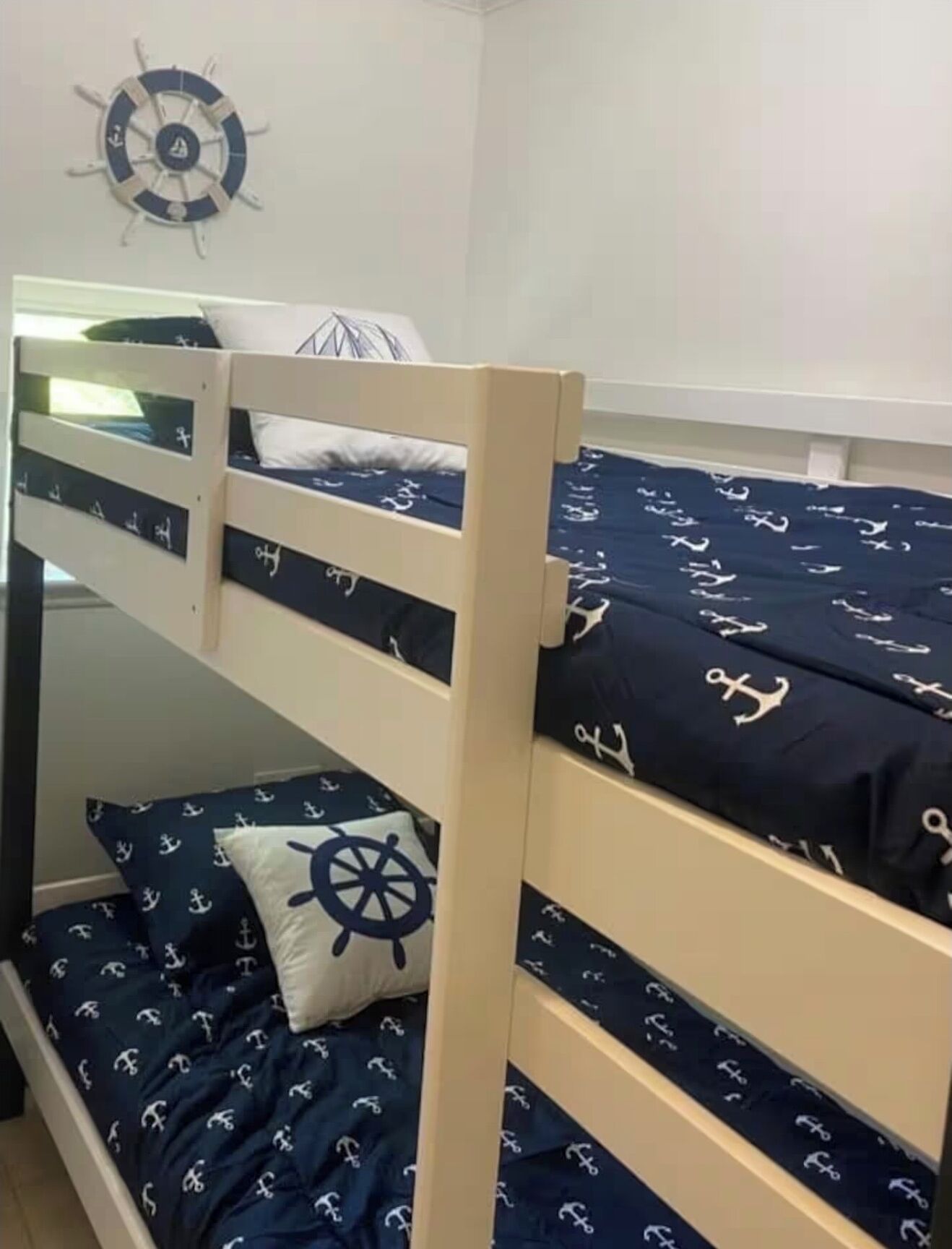 A bunk bed with navy bedding featuring anchor patterns, a ship's wheel pillow, and a wall clock.