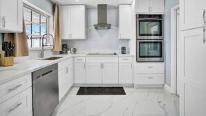 Een moderne keuken met witte kastjes, een vaatwasser, een dubbele oven en een raam met gordijnen.