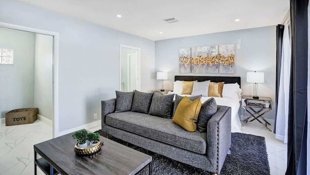 Een moderne hotelkamer met een grijze bank, een houten salontafel, een bed met witte lakens en een groot abstract schilderij aan de muur.