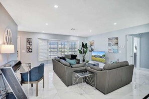 A modern living room with a sectional sofa, a glass coffee table, and a flat-screen TV. - Stunning 4BR Hted Pool &Jacuzzi Close 2 the Beach (Deerfield Beach)