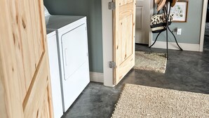 Une buanderie avec un lave-linge et un sèche-linge blancs, une porte en bois et un sol noir.