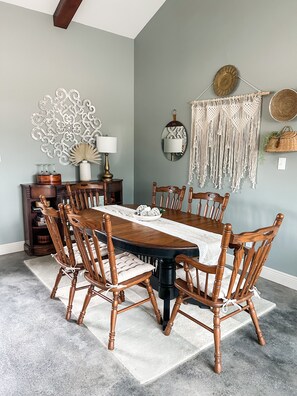 Un comedor con una mesa y sillas de madera, un adorno en la pared y un colgador de macramé.