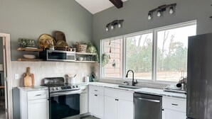 Une cuisine moderne avec des armoires blanches, un réfrigérateur en acier inoxydable et une grande fenêtre offrant une vue sur l’extérieur.