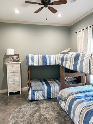 Una cama individual con ropa de cama a rayas, un aparador con cajones, una lámpara y un ventilador de techo.