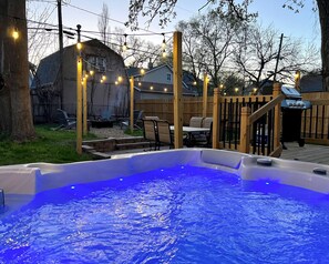 A backyard with a hot tub, wooden deck, outdoor furniture, and string lights. - The CORN CRIB: Spa - Game Room - BBQ - Office - DOWNTOWN - Sleeps 14 (Des Moines)