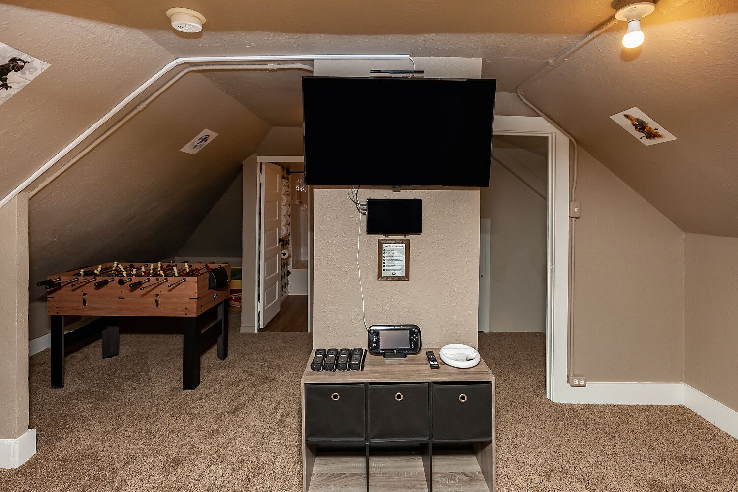 A cozy attic room with a foosball table, a TV mounted on the wall, and a small cabinet with drawers.