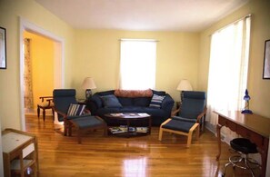 Una sala de estar con un sofá azul oscuro, dos sillones, una mesita de centro y una lámpara sobre una mesita auxiliar de madera.