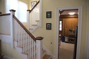 A staircase with white railings and a wooden handrail, leading to a landing with framed pictures on the wall. - Comfortable light-filled, 1920's home w/EV Charger  (Utica)