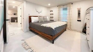 A bedroom with a bed, bedside tables, a wardrobe, and a bathroom visible through an open door. - Luxury Sea Cabin Guest Suite - Across from Beach (Folly Beach)