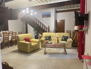 Uma sala de estar com um sofá amarelo, uma poltrona amarela, uma mesa de centro e uma área de jantar com mesa e cadeiras.