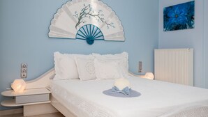 A bedroom with a bed, white bedding, a decorative wall hanging, a bedside table, and a wall-mounted radiator.