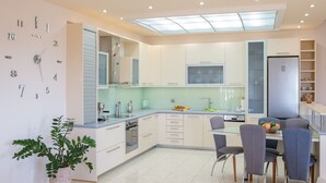 A modern kitchen with a dining area, featuring a clock on the wall, a large window, and a built-in oven.
