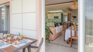 A dining area with a table set for a meal, a kitchen in the background, and a living area with a sofa and a chandelier.