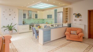 A modern kitchen with a central island, a dining area with a table and chairs, a sofa, and a potted plant.