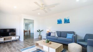 Ein modernes Wohnzimmer mit Flachbildfernseher, einem grauen Sofa, einem Holztisch und einem Deckenventilator.