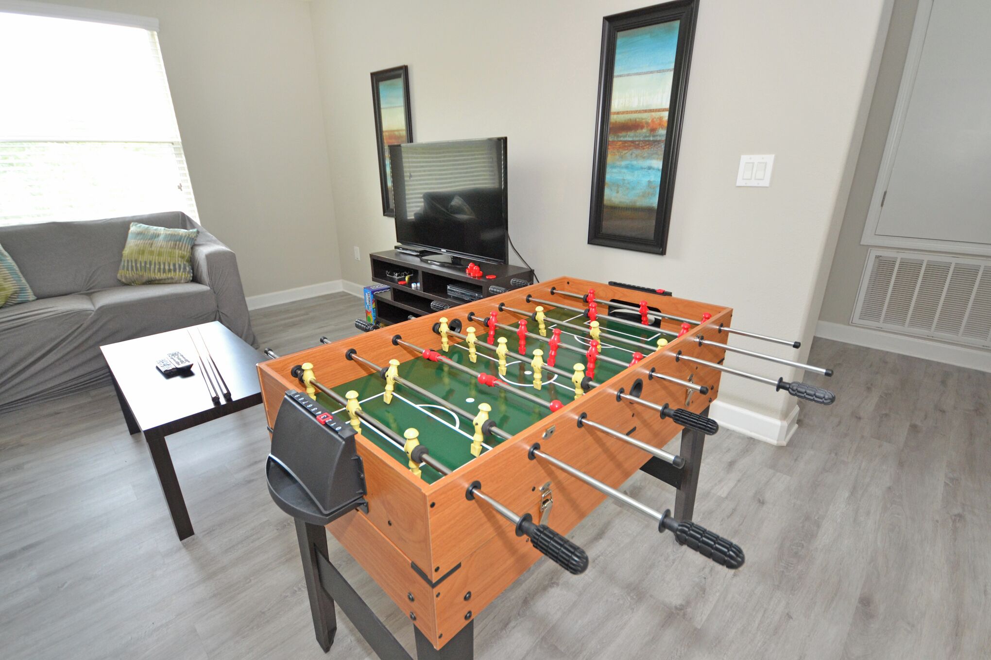 A living room with a foosball table, a sofa, a coffee table, and a television.
