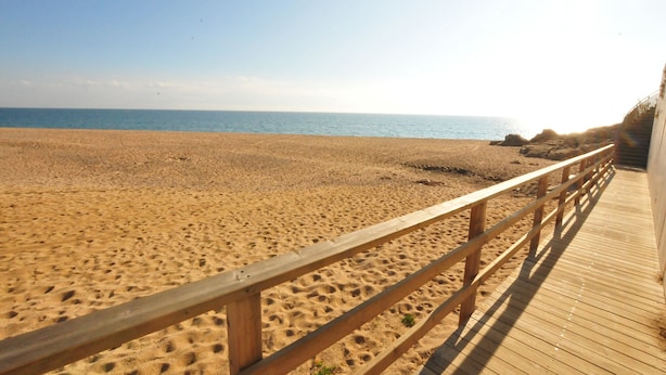 Une plage de sable avec une promenade en bois menant à un bâtiment.