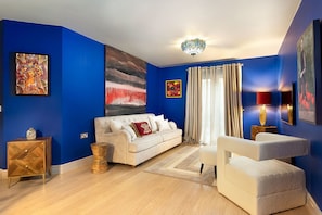 A living room with a blue wall, a white sofa, a small side table, a decorative lamp, and a floor lamp.