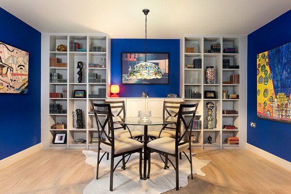 A dining area with a round table and four chairs, surrounded by white shelving units filled with books and decorative items.