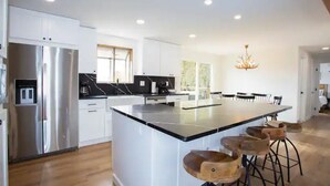 A modern kitchen with white cabinetry, a stainless steel refrigerator, a large island with bar stools, and recessed ceiling lighting. - Kid and Dog Friendly Home w/ Amazing Views! (Glenwood Springs)