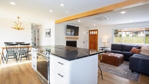 A modern kitchen with a central island, a dining area with chairs, a sofa, and a TV. - Kid and Dog Friendly Home w/ Amazing Views! (Glenwood Springs)