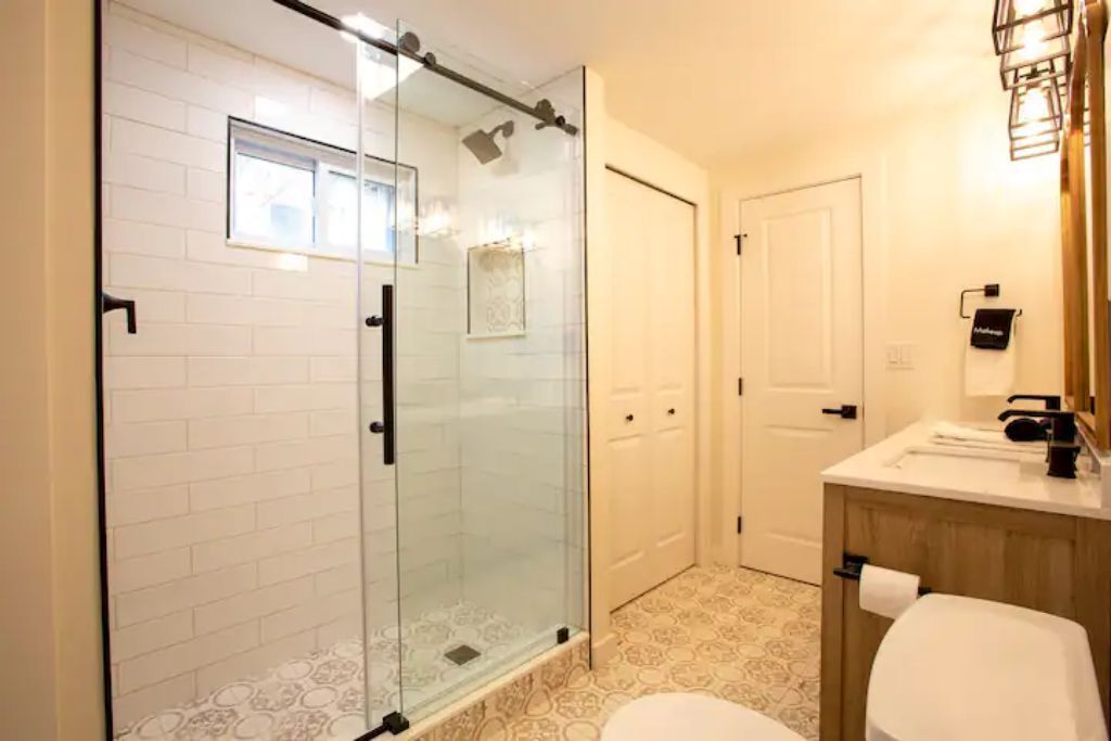 A bathroom with a glass shower enclosure, a white toilet, and a wooden vanity with a mirror.