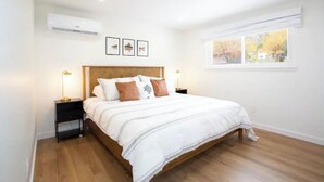 A bedroom with a wooden bed, white bedding, a nightstand with a lamp, and a window with a view of trees. - Kid and Dog Friendly Home w/ Amazing Views! (Glenwood Springs)
