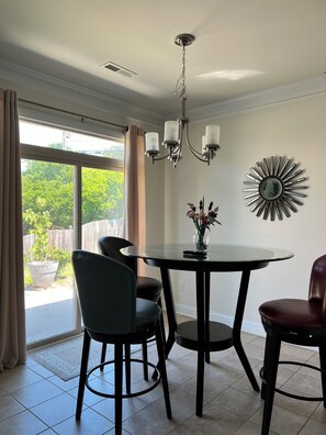 A dining area with a round table, four chairs, a chandelier, and a decorative wall piece.