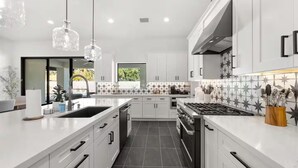 A modern kitchen with white cabinets, a central island, a stove, and pendant lighting. - Querencia  | Pool, Hot Tub, Putting Green, Fire Pit, TPC Golf | Scottsdale (Scottsdale)