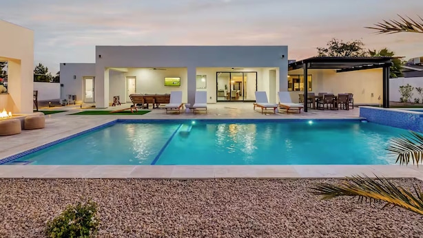 A modern outdoor pool area with a rectangular pool, lounge chairs, and a covered seating area. - Querencia  | Pool, Hot Tub, Putting Green, Fire Pit, TPC Golf | Scottsdale (Scottsdale)