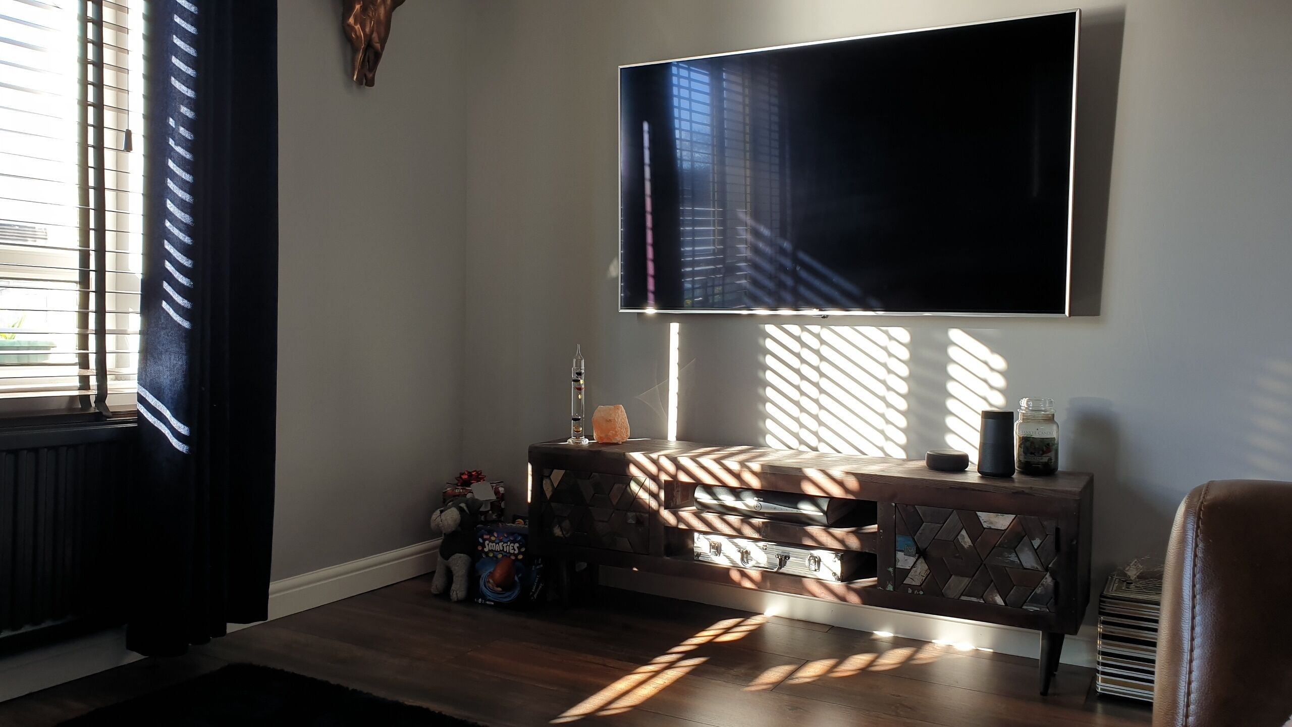 Una sala de estar con un televisor de pantalla plana montado en la pared, una mesa de centro de madera y una mesita auxiliar con una lámpara de sal y una vela.