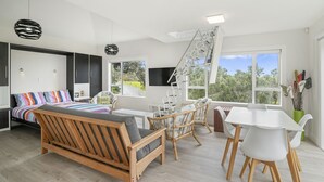 Un salon moderne comprenant un canapé, une table à manger et des chaises, un escalier et de grandes fenêtres donnant sur un paysage verdoyant.