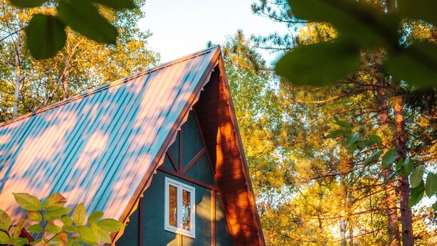 Een chalet met een steile dakschild, een houten terras en een veranda met een bank.