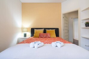 A hotel room with a bed, two pillows, a nightstand with a lamp, and a door leading to another room. - Rustic Central Flat | Terrace by Host Wise (Porto)
